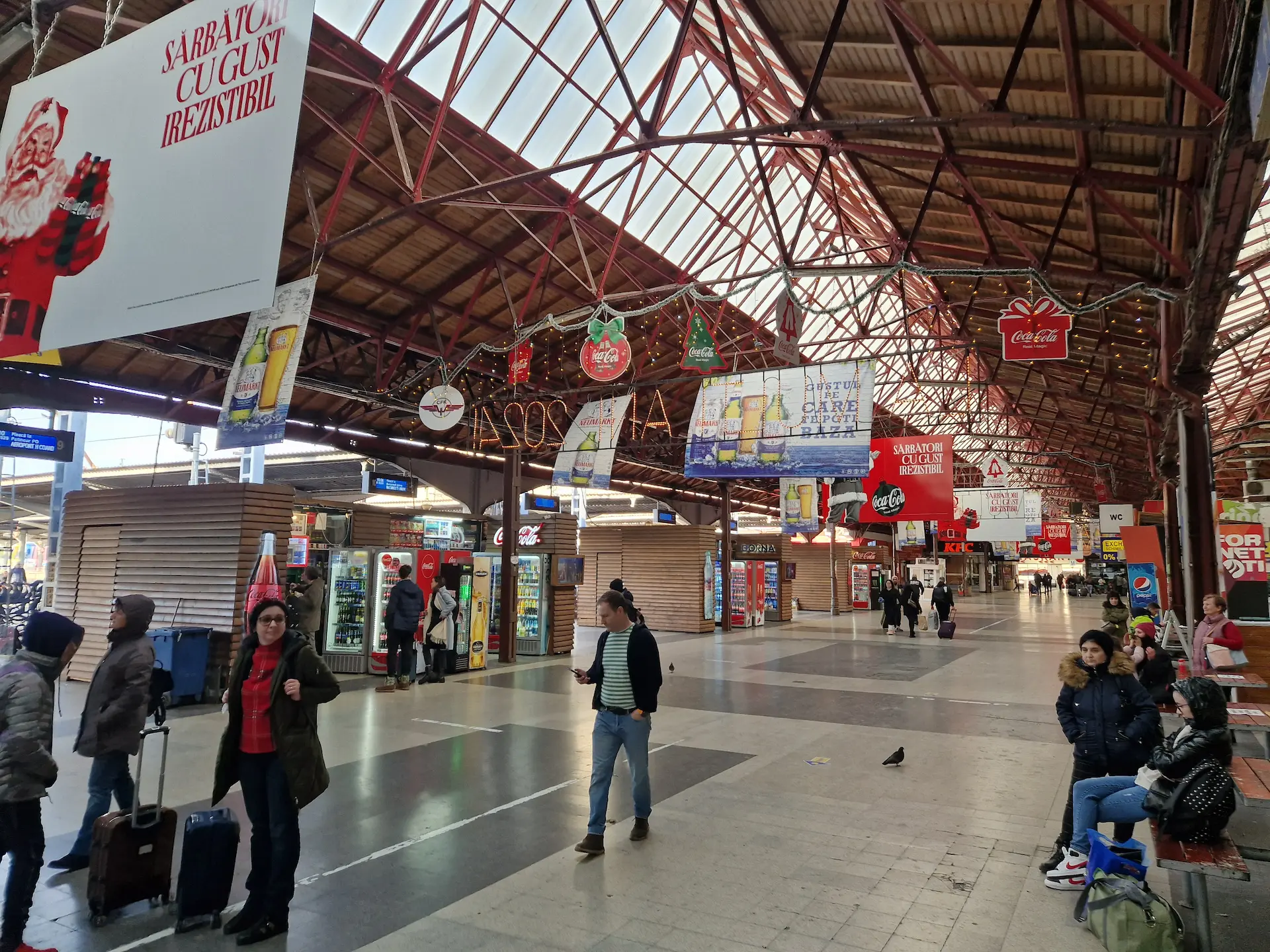 Hall de gare illuminé, des panneaux publicitaires et décorations de Noël pendent du plafond