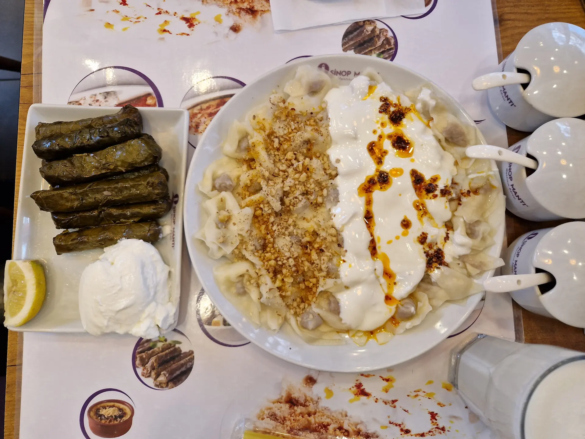 Deux plats vus d'en haut : des dolmas avec du yaourt et un quartier de citron, une assiette de mantı dont chaque moitié est aggrémentée de différents ingrédients.