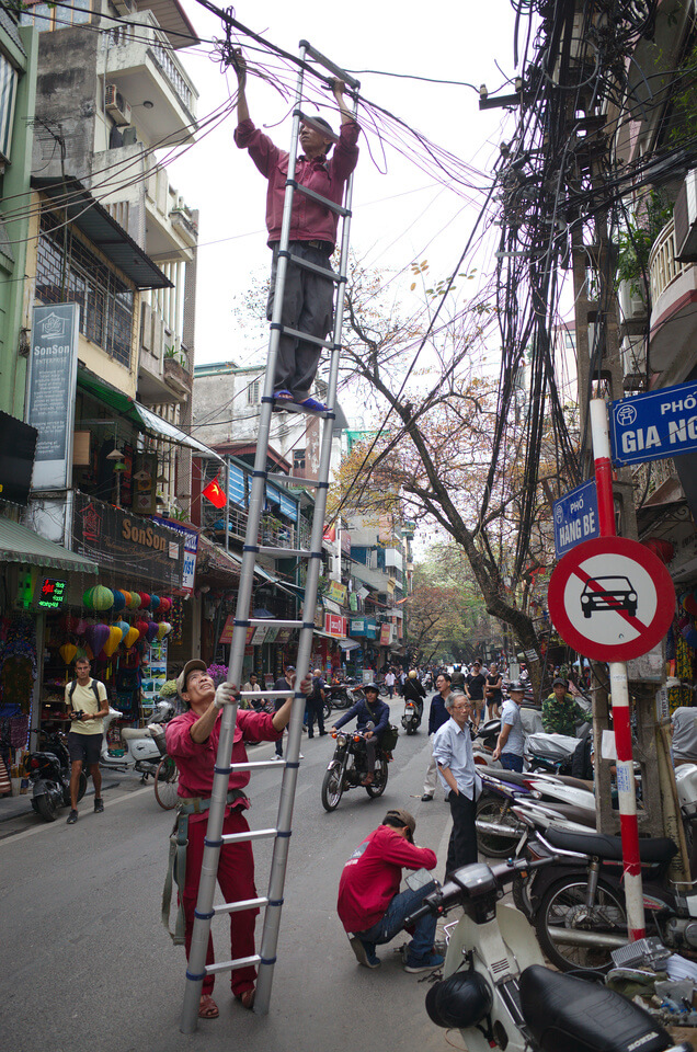 Un électricien perché sur une échelle coupe des fils électriques illégaux à Hanoï