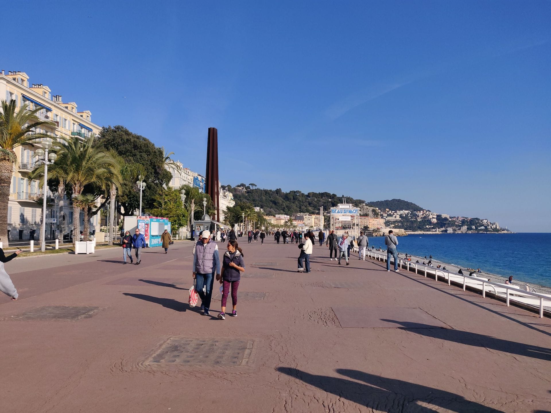 La promenade des Anglais à Nice, quai piéton qui longe la baie. Il y a du soleil et des promeneurs