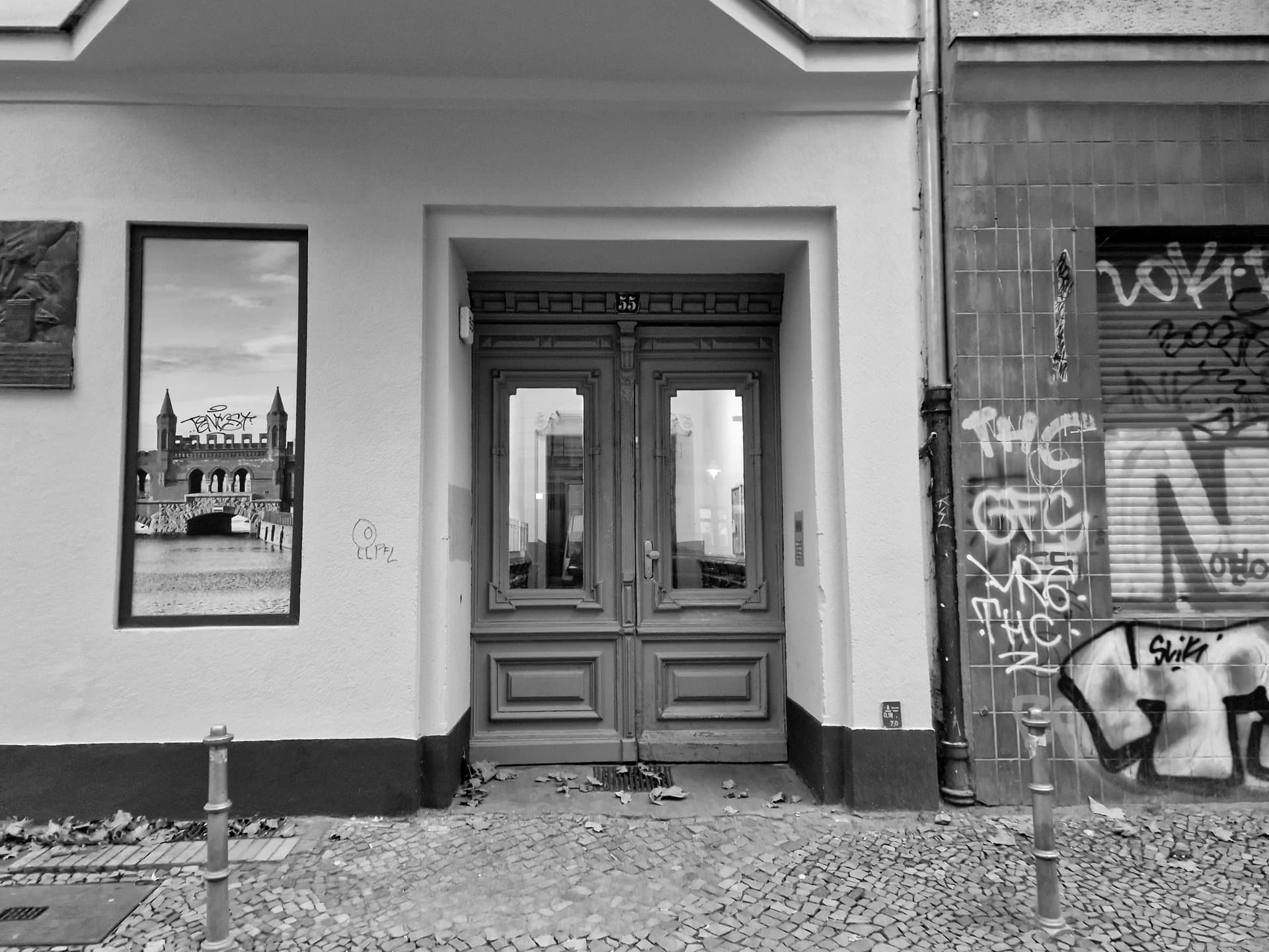 Porte d'entrée de Dieffenbachstraße 55 : quelques graffitis sur la droite, une fenêtre recouverte d'un faux paysage sur la gauche.