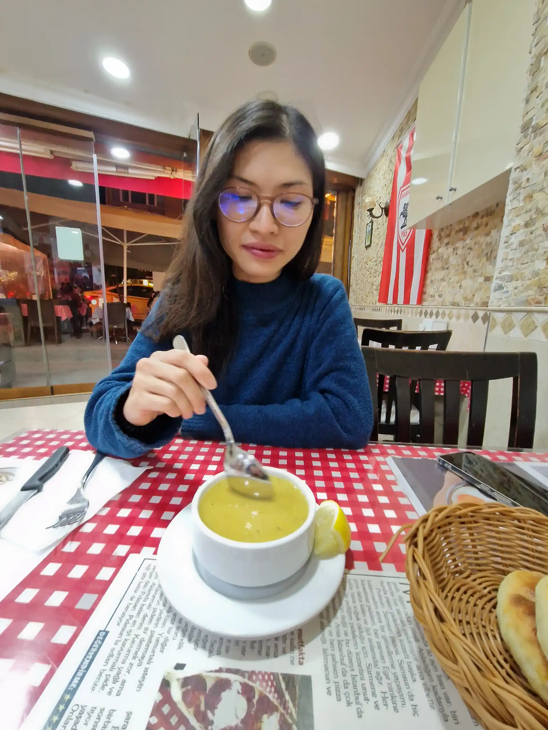 Clara mange une soupe aux lentilles. La soupe est jaune et servie avec un quartier de citron sur le côté.
