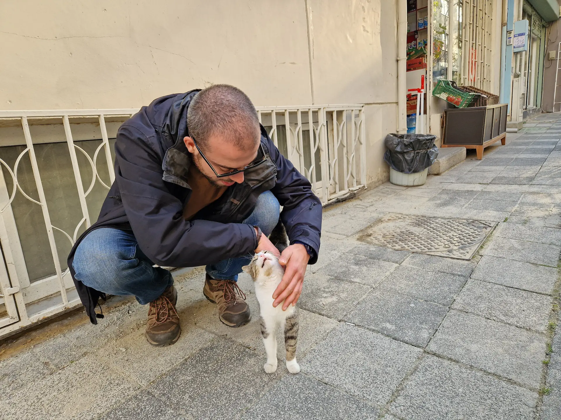 Robin caresse un tout petit chat (qui a l'air de beaucoup aimer) sur un trottoir de Kadıköy