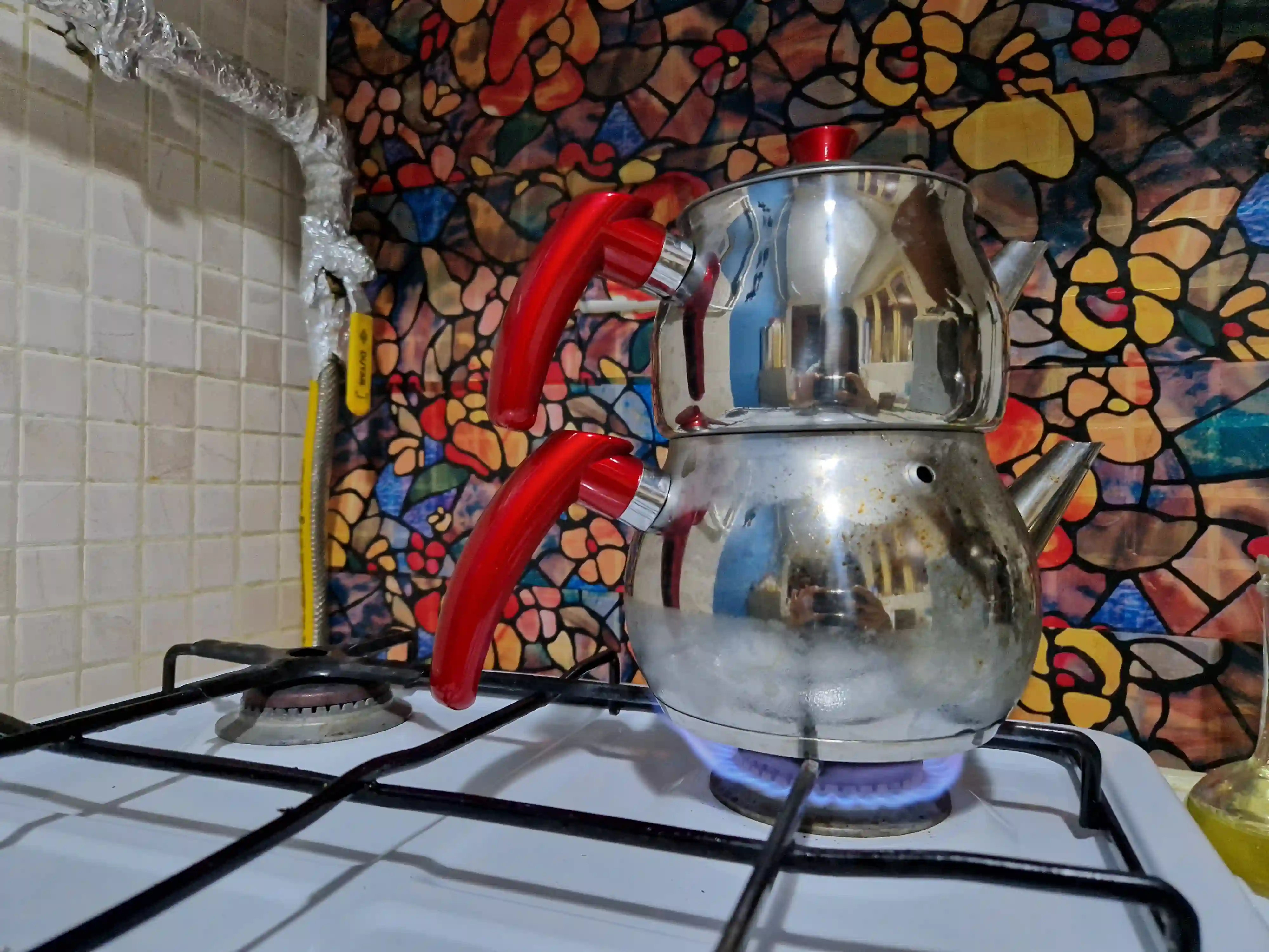 Une théière en métal à deux étages chauffe sur le feu à gaz d'une cuisinière.