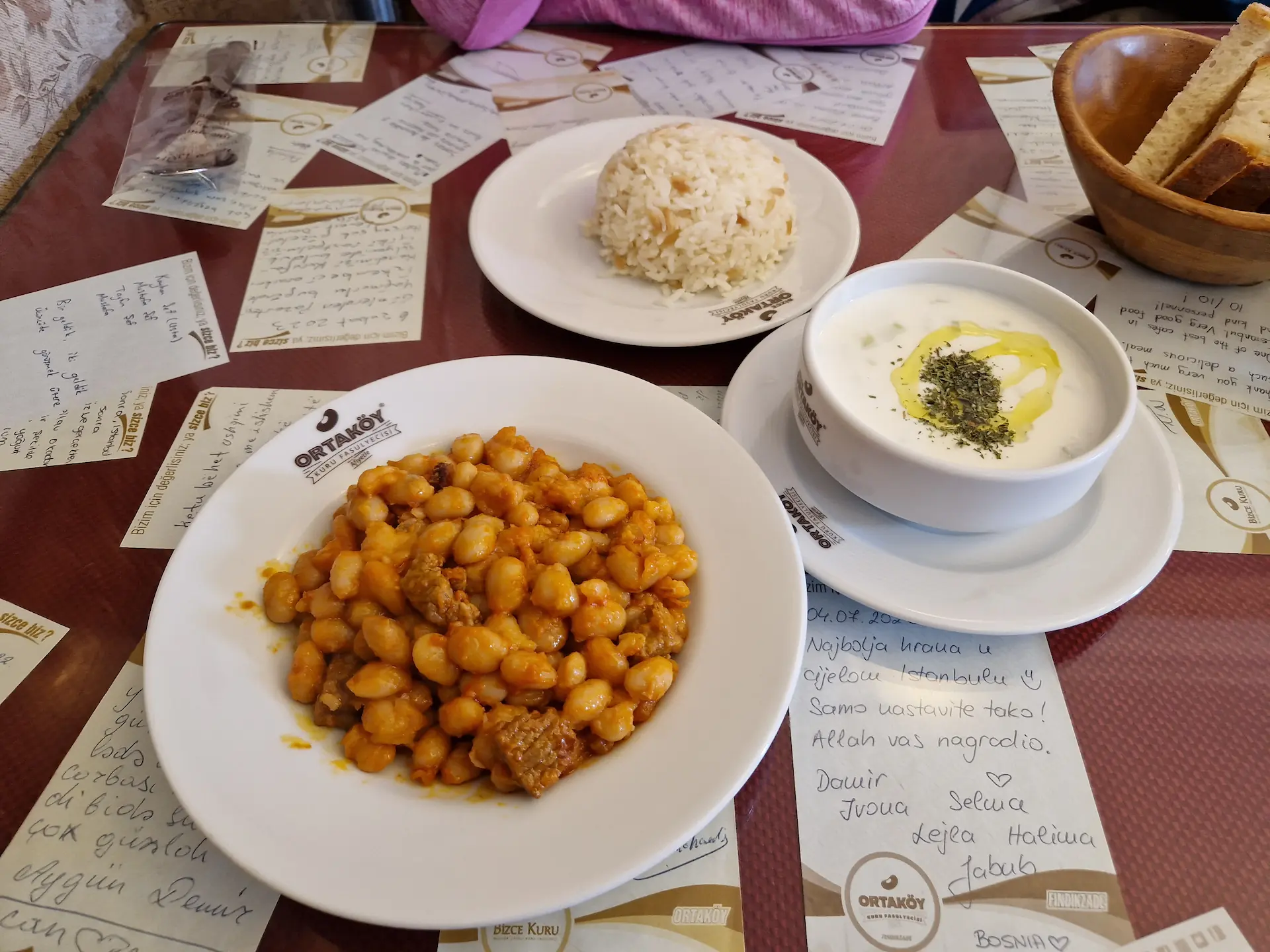 Sur la table d'un restaurant, un plat de kuru fasulye (haricots blancs à la viande et sauce tomate), accompagné de riz et de yaourt.