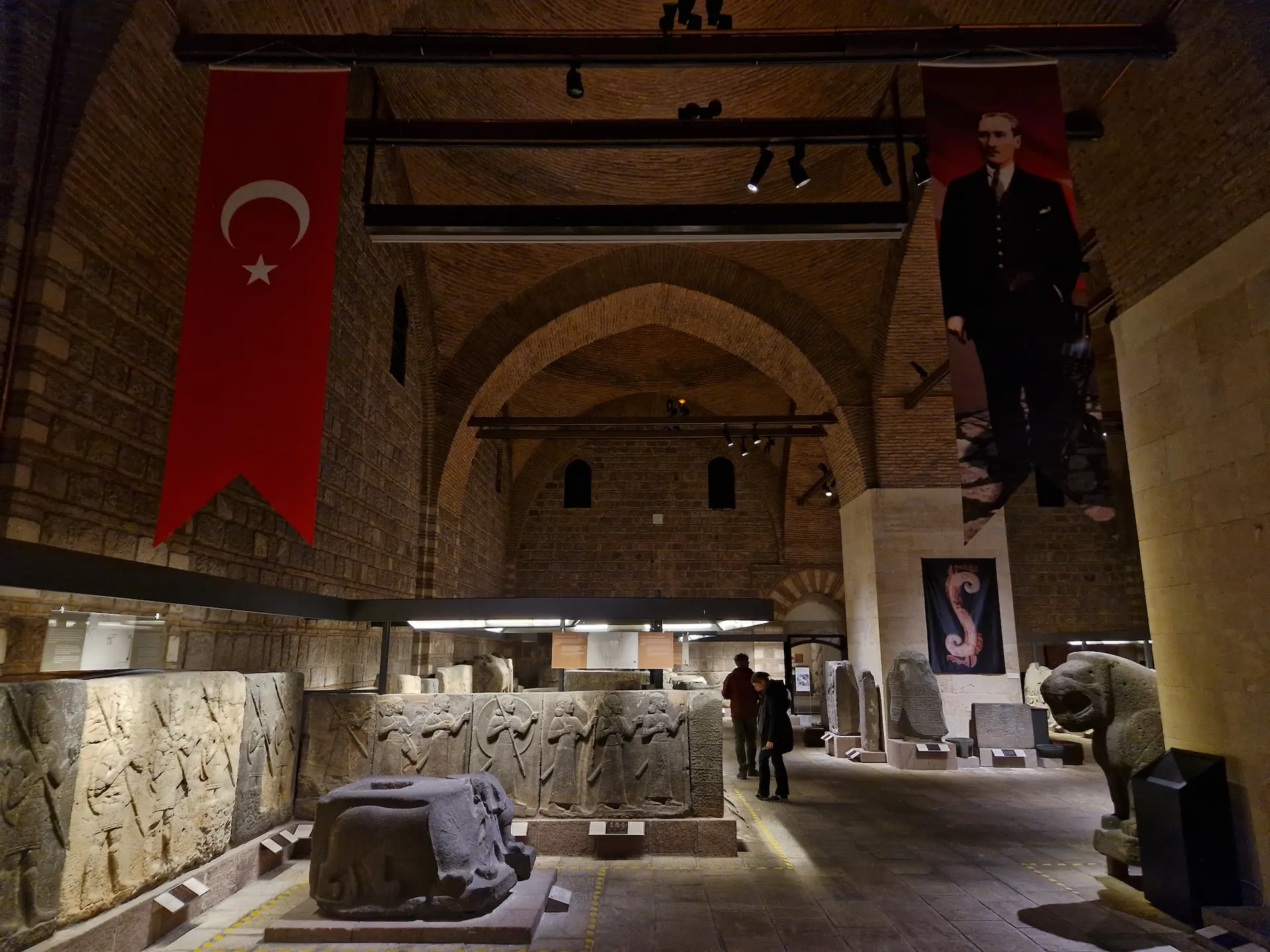La salle centrale du musée. Sur le sol, des statues et sculptures. On voit des bannières accrochées au plafond avec sur la première, le drapeau turc, et sur la deuxième, un portrait d'Atatürk.