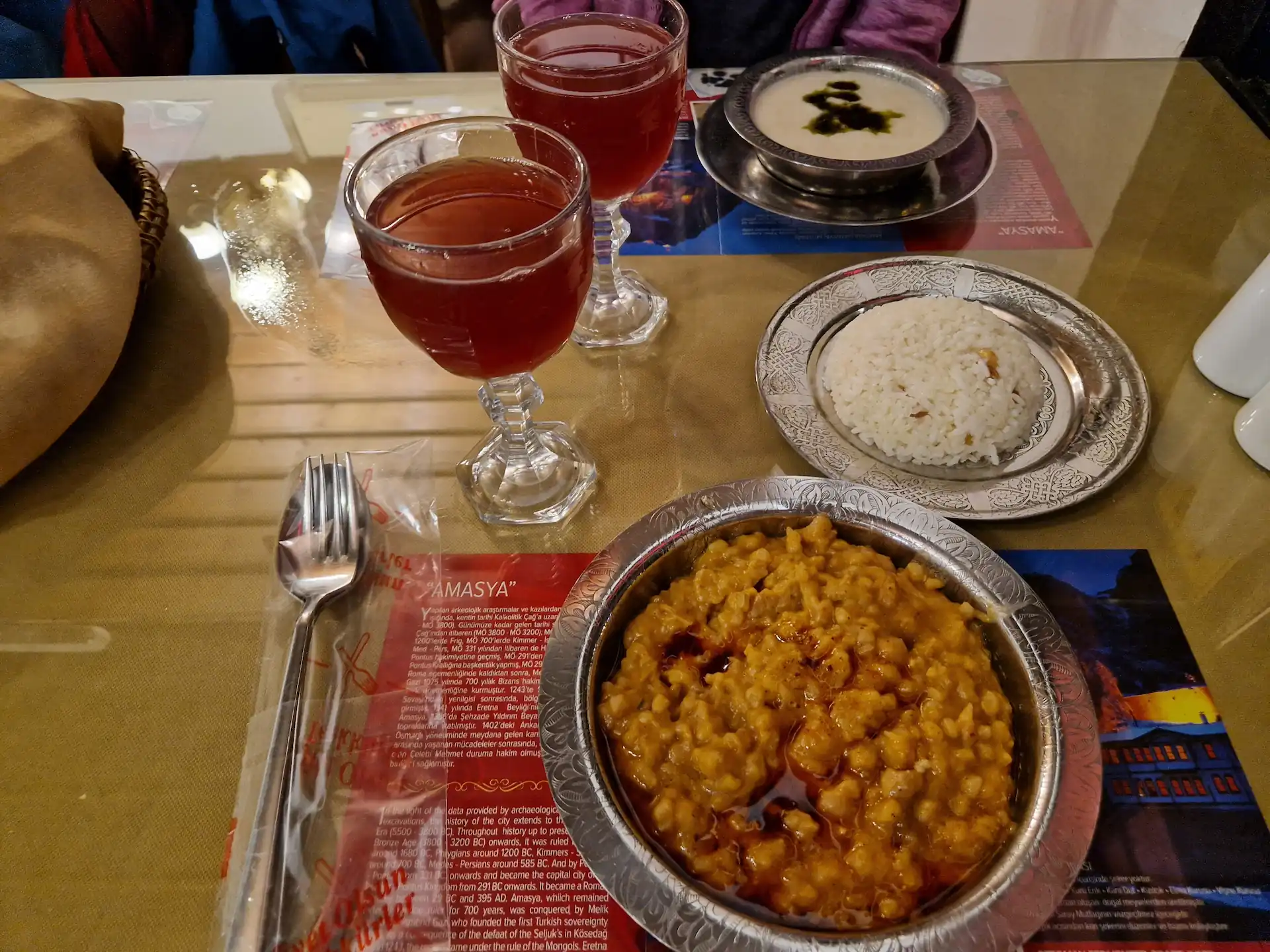 Sur une table, trois plats sont disposés : une soupe blanche, un plat de riz, un porridge à la couleur presque orange. Il y a également deux verres à pied où sont servis des jus aux épices.