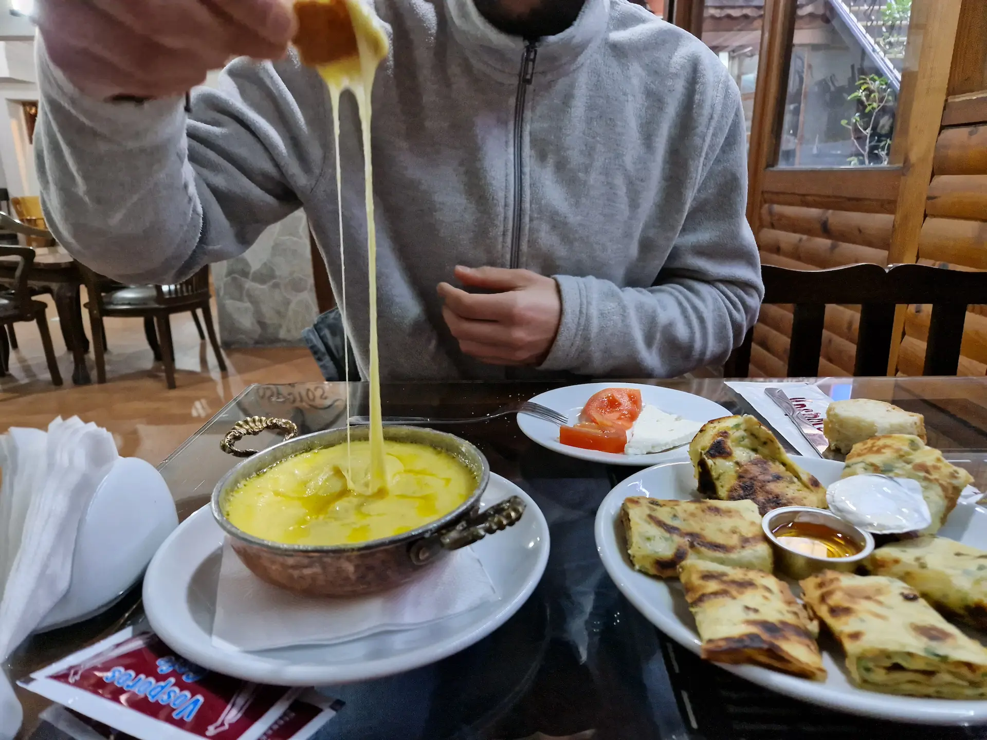 Robin trempe un morceau de pain dans une muhlama pour un petit-déjeuner à Trabzon. Le fromage fait plein de fils. On voit une assiette de kaygana sur le côté.