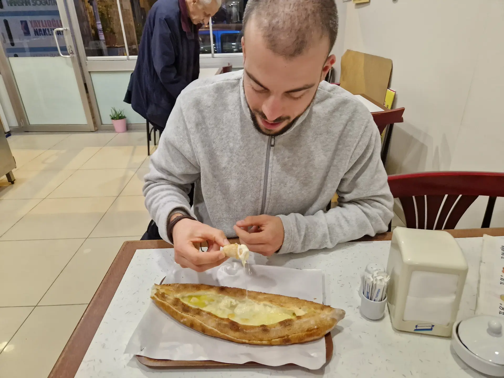 Robin entame une pide au fromage dans un petit resto de pide à Trabzon. Il sourit légèrement en plongeant son pain dans le mélange de fromage et de beurre.