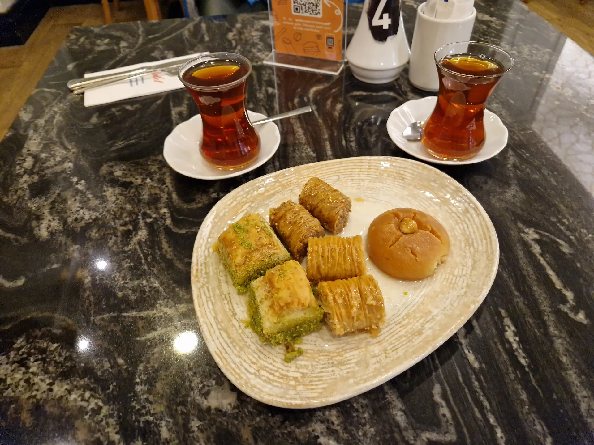 Sur une table, deux petites tasses de thé turc et une assiette avec quatre sortes de baklava différentes.