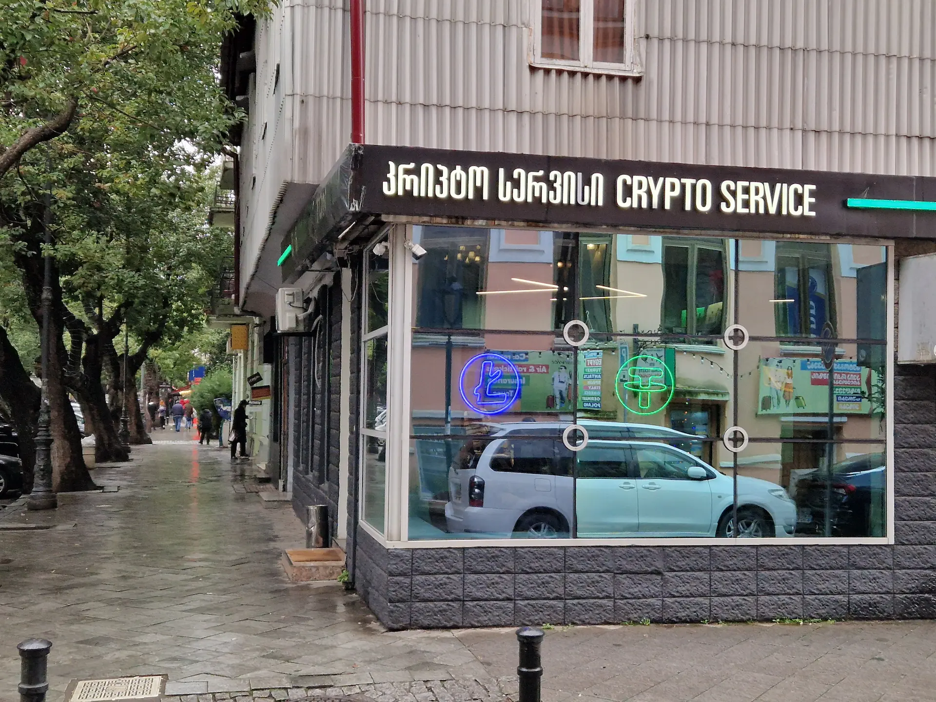 Un commerce dans un boulevard de Batoumi bordé d'arbres, on y lit 'Crypto Service' en anglais et en géorgien.