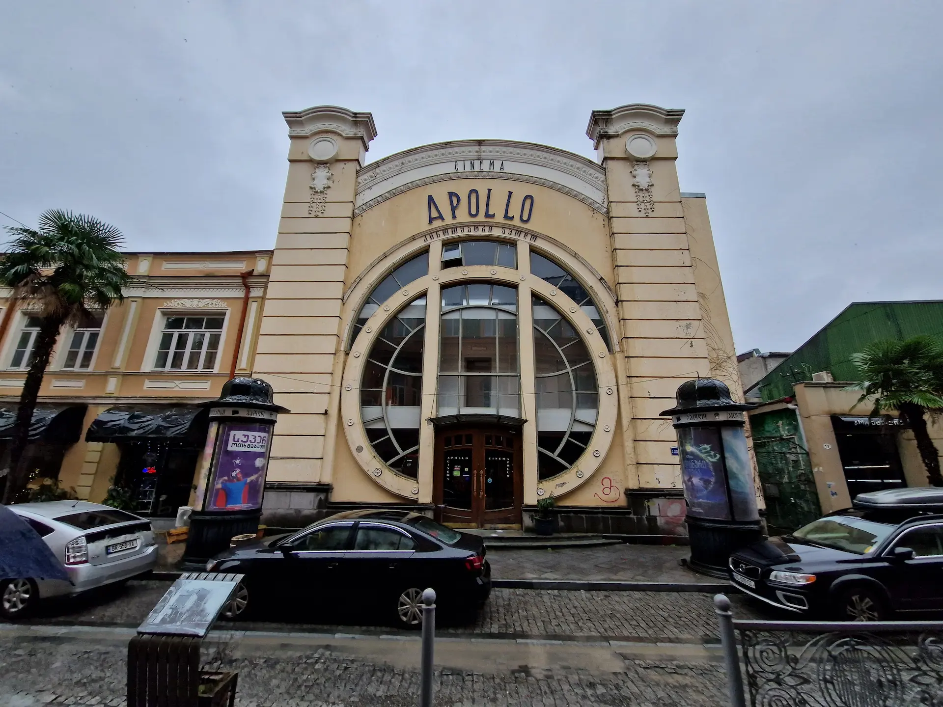 Le cinéma Apollo à Batoumi. La façade est percée par une énorme baie vitrée circulaire, et le haut du bâtiment répète la courbe du cercle. 'Cinema Apollo' est inscrit sur la façade dans un style très années 1920.
