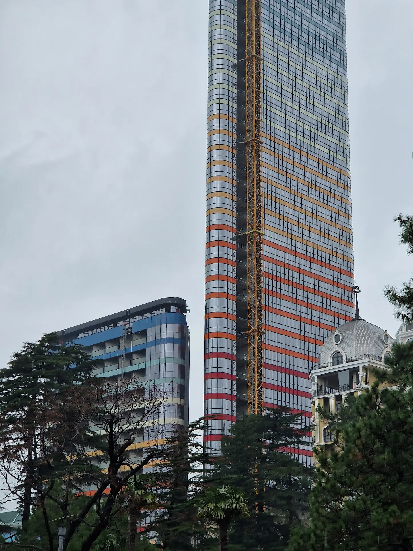 La nouvelle tour Azure de Batoumi, encore plus grande que le Marriott, une coupe triangulaire et un dégradé du rouge au bleu en s'éloignant du sol.