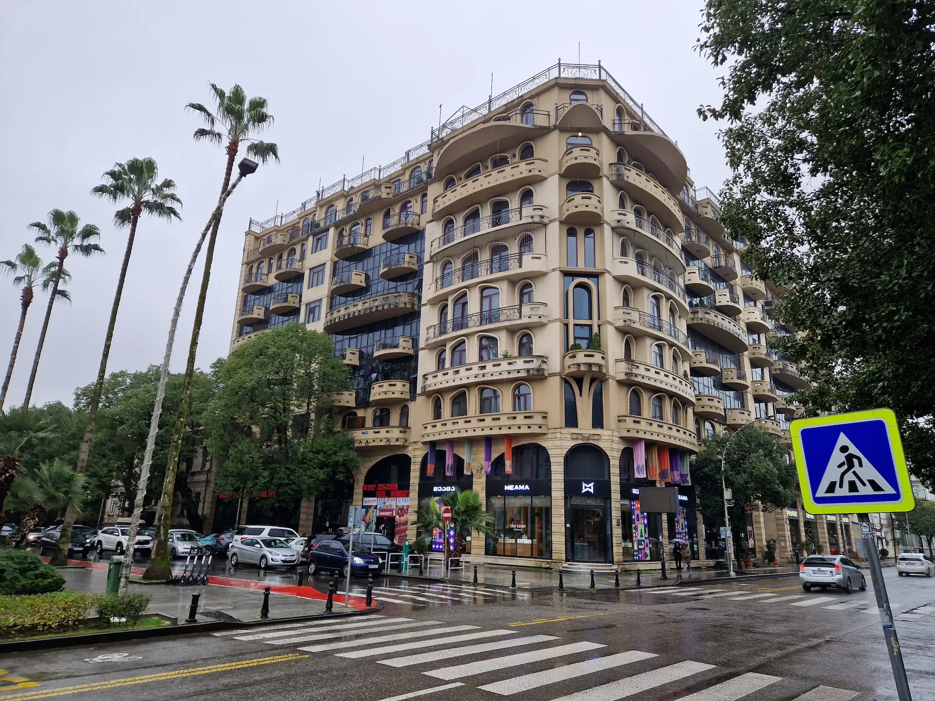 Un immeuble Art Nouveau le long d'un boulevard à Batoumi, tout en courbes arrondies. Quelques hauts palmiers se dressent en face.