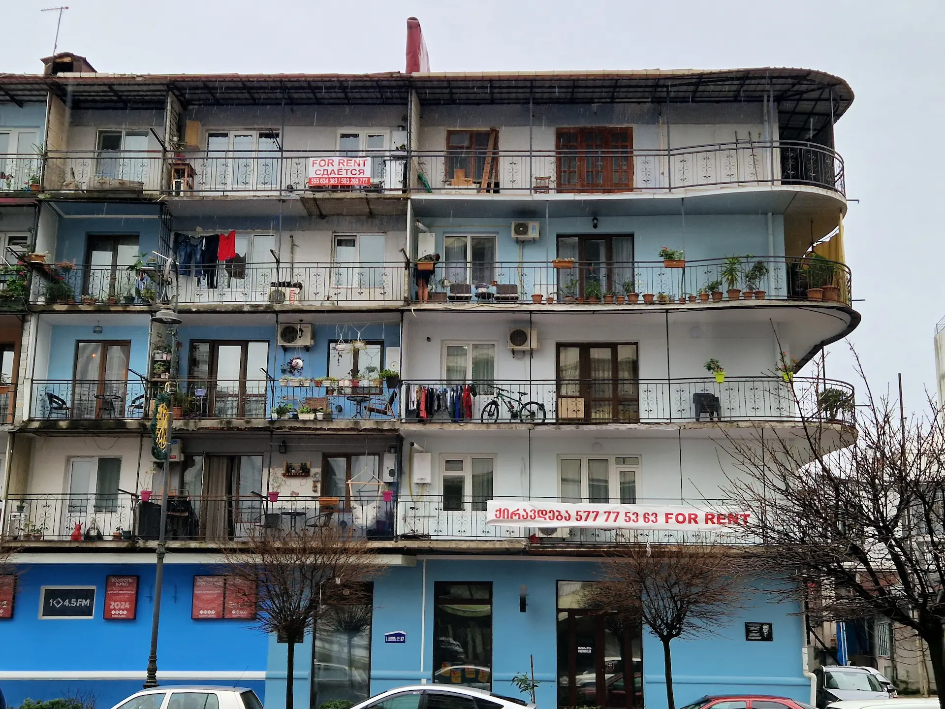 Un immeuble de quatre étages peint en différentes teintes de bleu, au coin arrondi, avec des balcons communiquants et couverts où sèchent des habits.