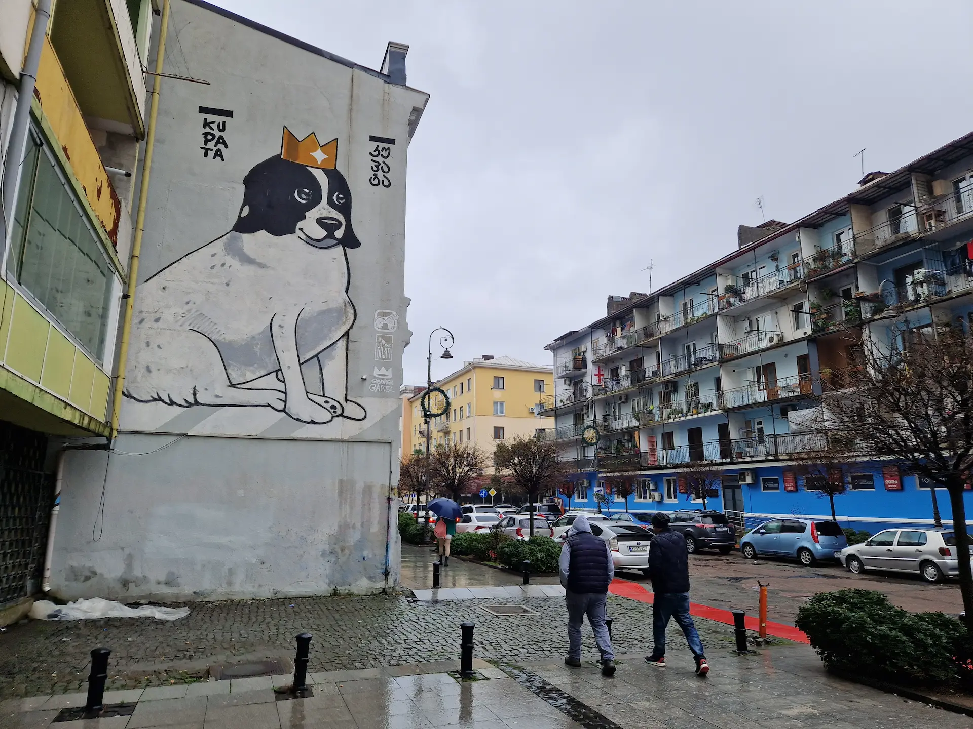 Sur la façade d'un immeuble à Batoumi, une murale d'un chien blanc et noir avec une couronne sur la tête. Le nom du chien est écrit en alphabet latin et géorgien : Kupata