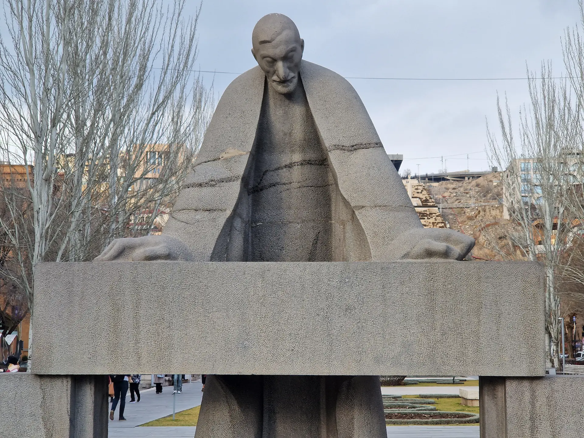 Statue d'Alexander Tamanyan, style brutaliste, taillé dans une pierre claire. La taille de ses bras est exagérée, se terminant en mains immenses, posées sur une table. Il regarde vers le bas, l'air penseur.