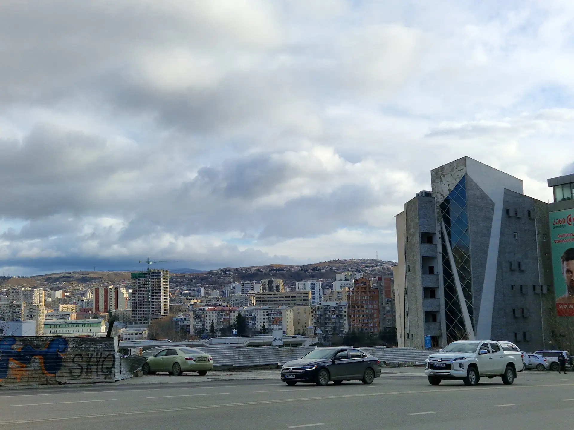 Une grande route devant nous, sur la droite un bâtiment moderne tout en verre. Au loin, des quartiers entiers de khrouchtchevkas.