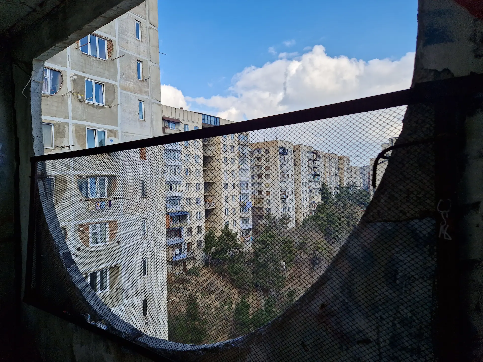 À travers une ouverture en demi-cercle, on aperçoit un bloc de bâtiments soviétiques.