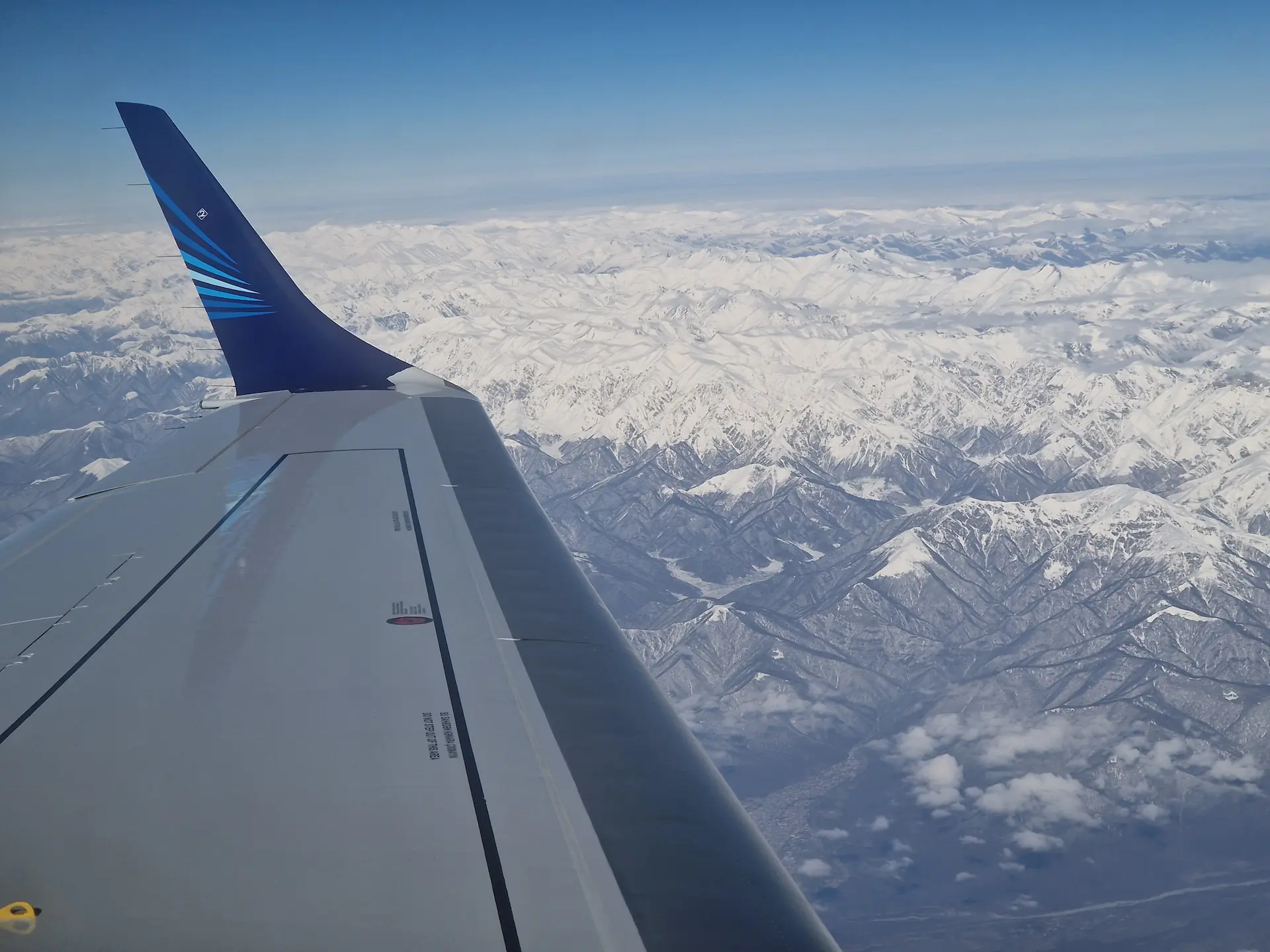 Vue de l'avion : le ciel est bleu, les montagnes du Caucase, blanches au sommet couvrent le sol.