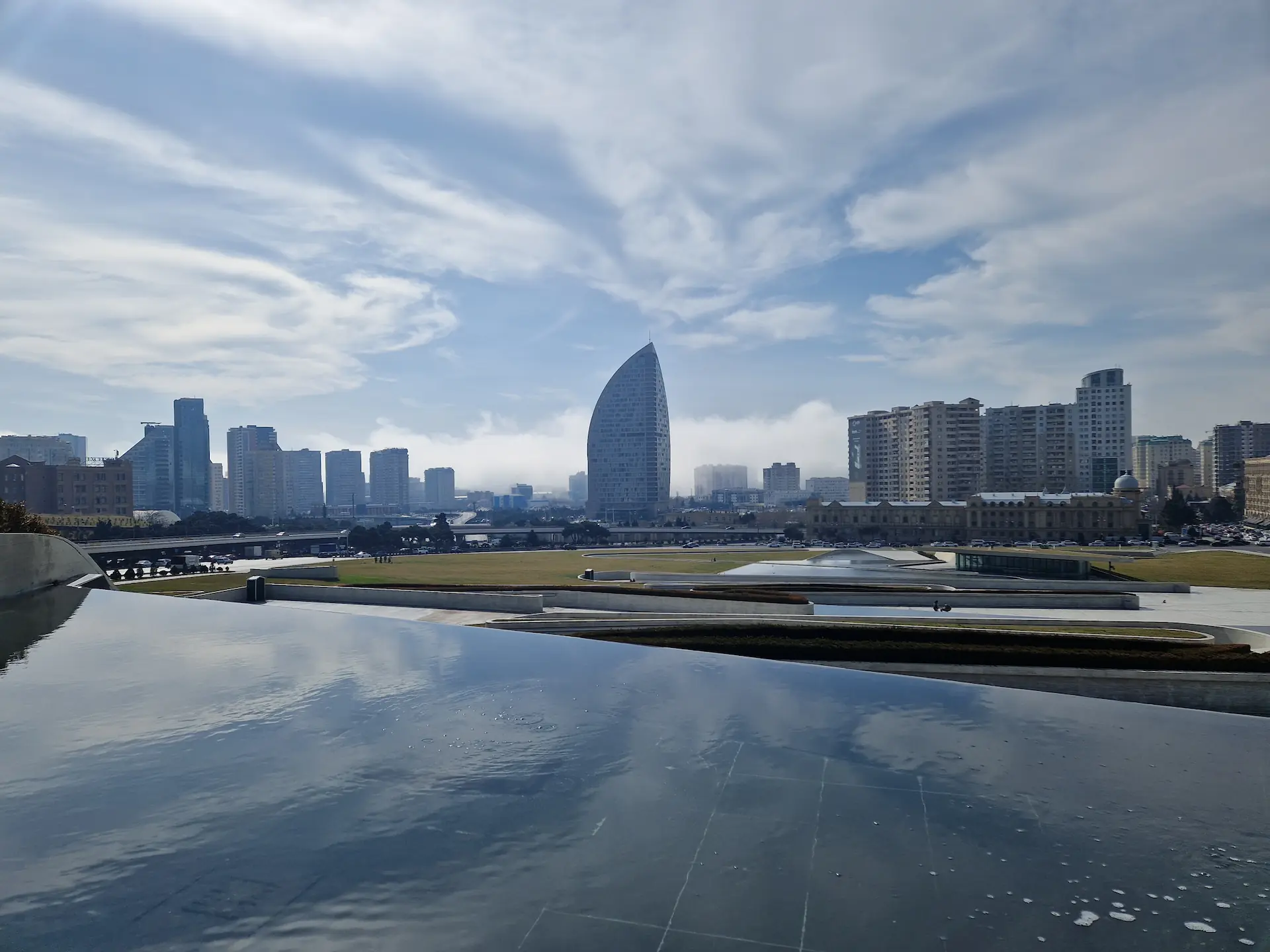 La ville de Bakou au loin, recouverte d'un nuage à ras le sol. Le ciel est bleu et ensoleillé.