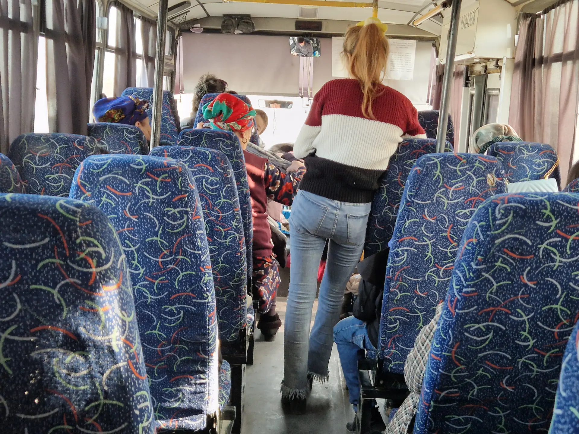 On est assis à l'arrière du bus et on voit les passagères à l'avant : deux grand-mères aux foulards colorés sur la tête et une jeune femme debout dans le couloir.