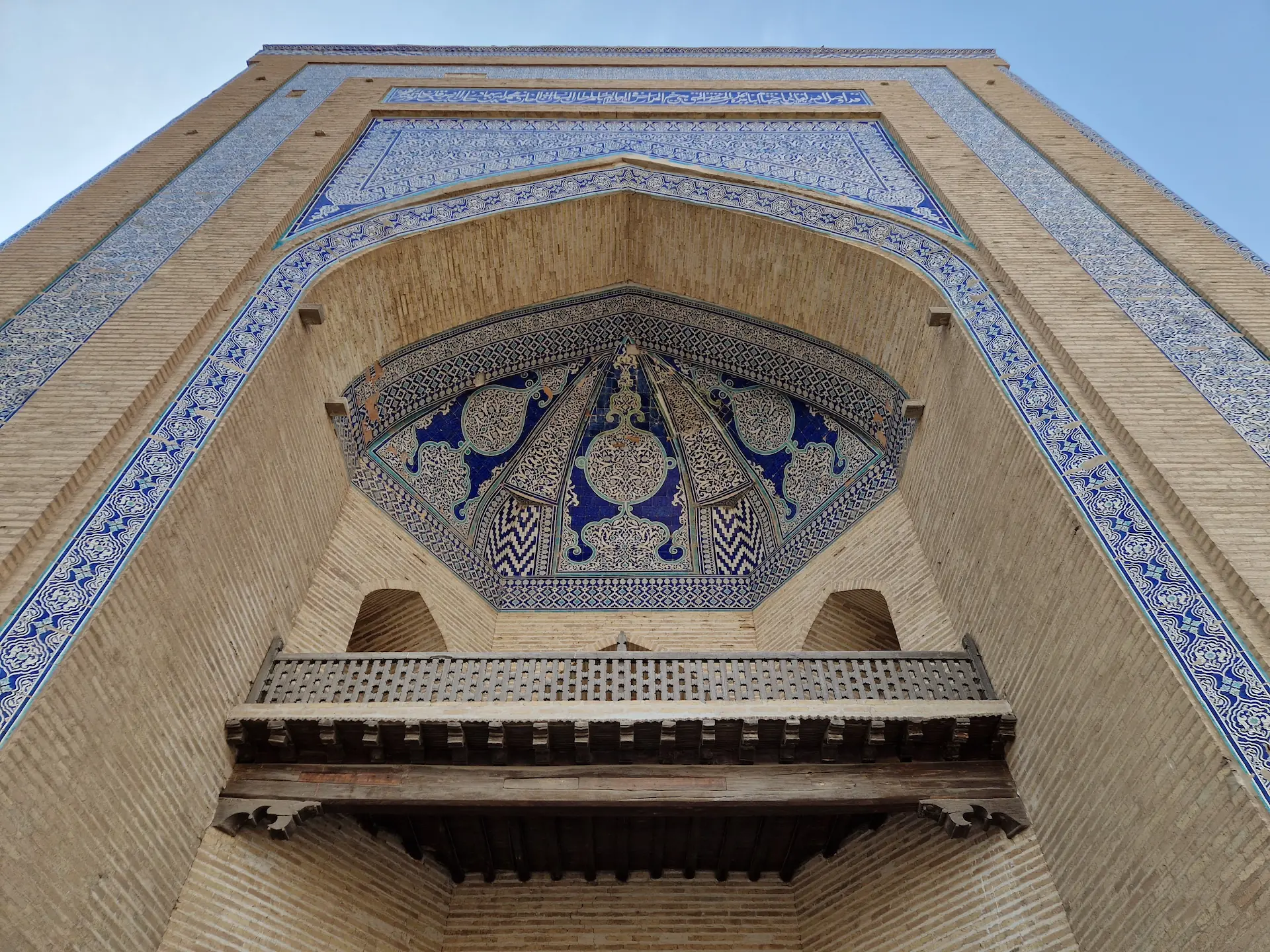 Entrée de la madrassa, vue d'en bas. Le bâtiment est en pierre et décoré de magnifiques morifs bleus et blancs.