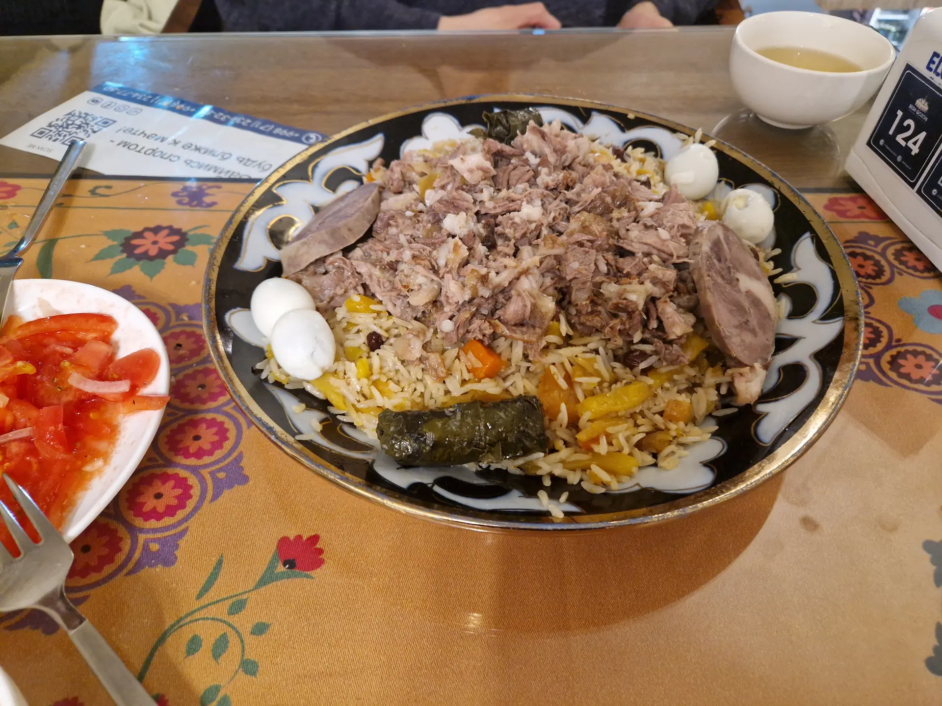 Une assiette de plov ouzbek : riz blanc en-dessous, carottes jaunes et viande par dessus, ici servi avec deux petits œufs de caille et deux feuilles de vigne farcies