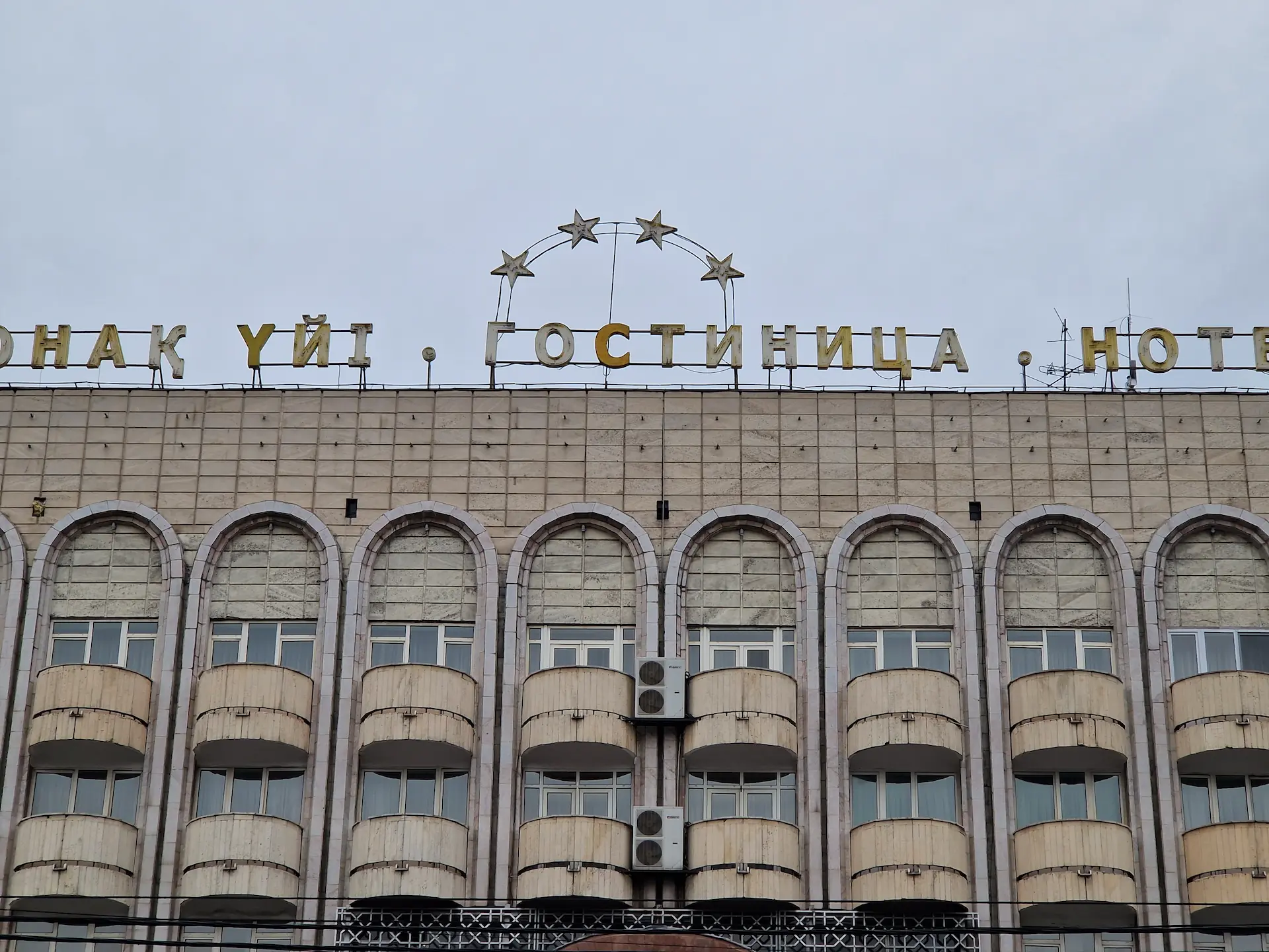 Détail d'un hôtel, la façade est entièrement en béton et adornée de petits balcons ronds, le nom de l'hôtel est indiqué en lettres décolorées sur le toit