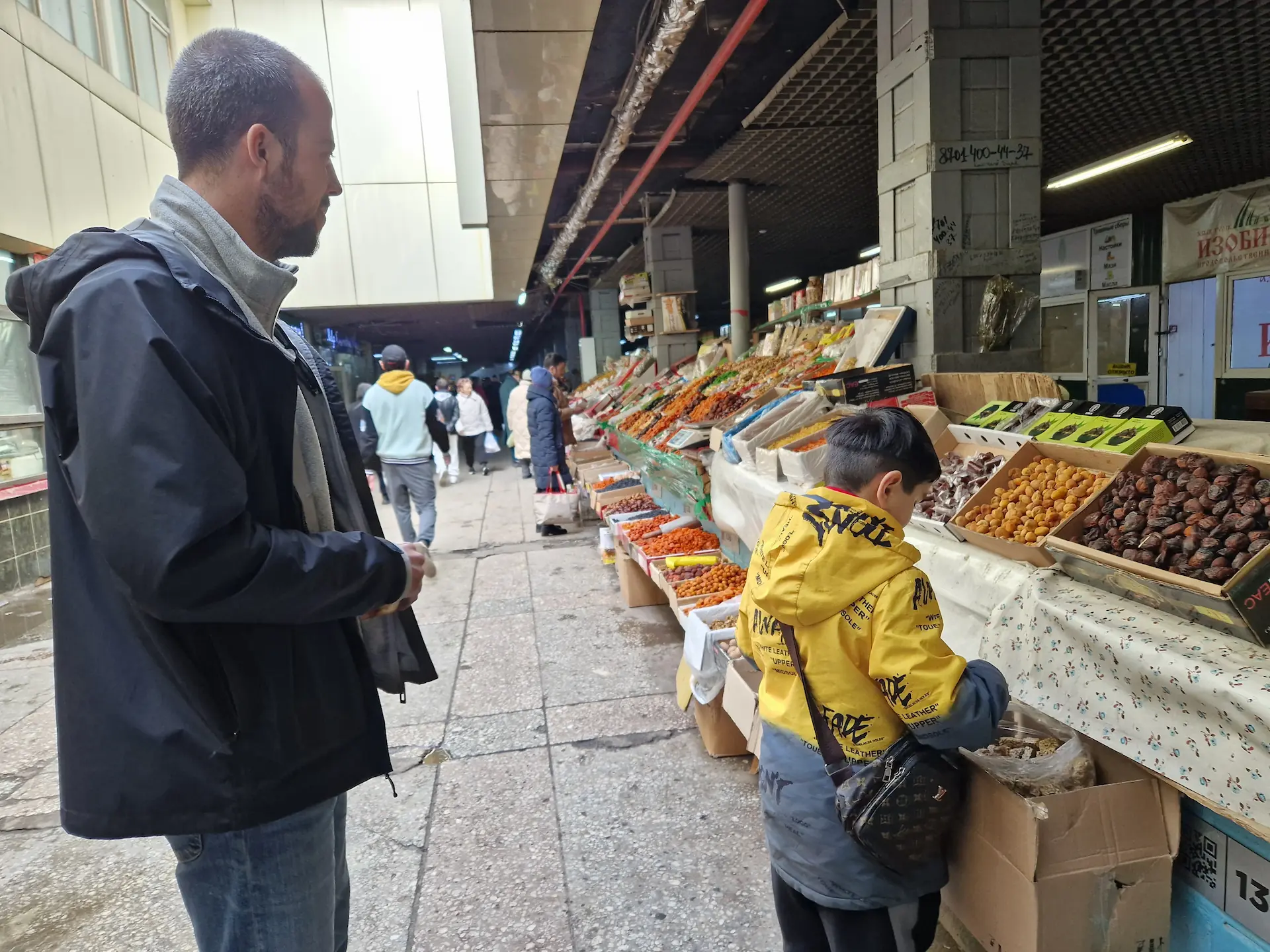 Robin achète des barres de céréales à un stand de fruits secs et noix, et se fait servir par un petit enfant