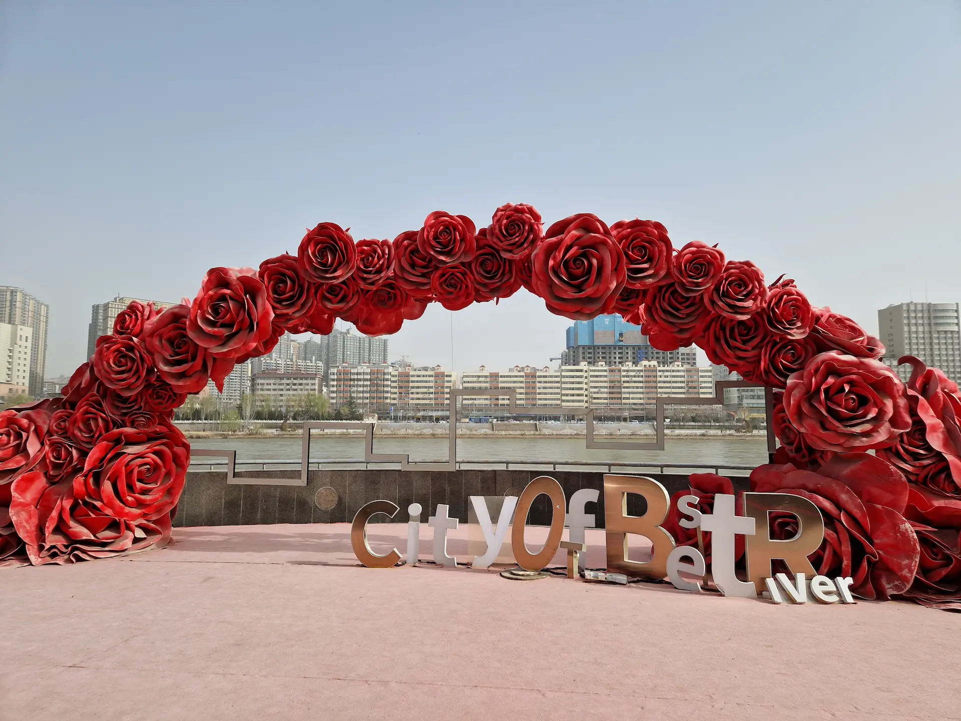 Une décoration de fausses fleurs rouges au bord du fleuve Jaune, avec l'inscription "City of Best River""