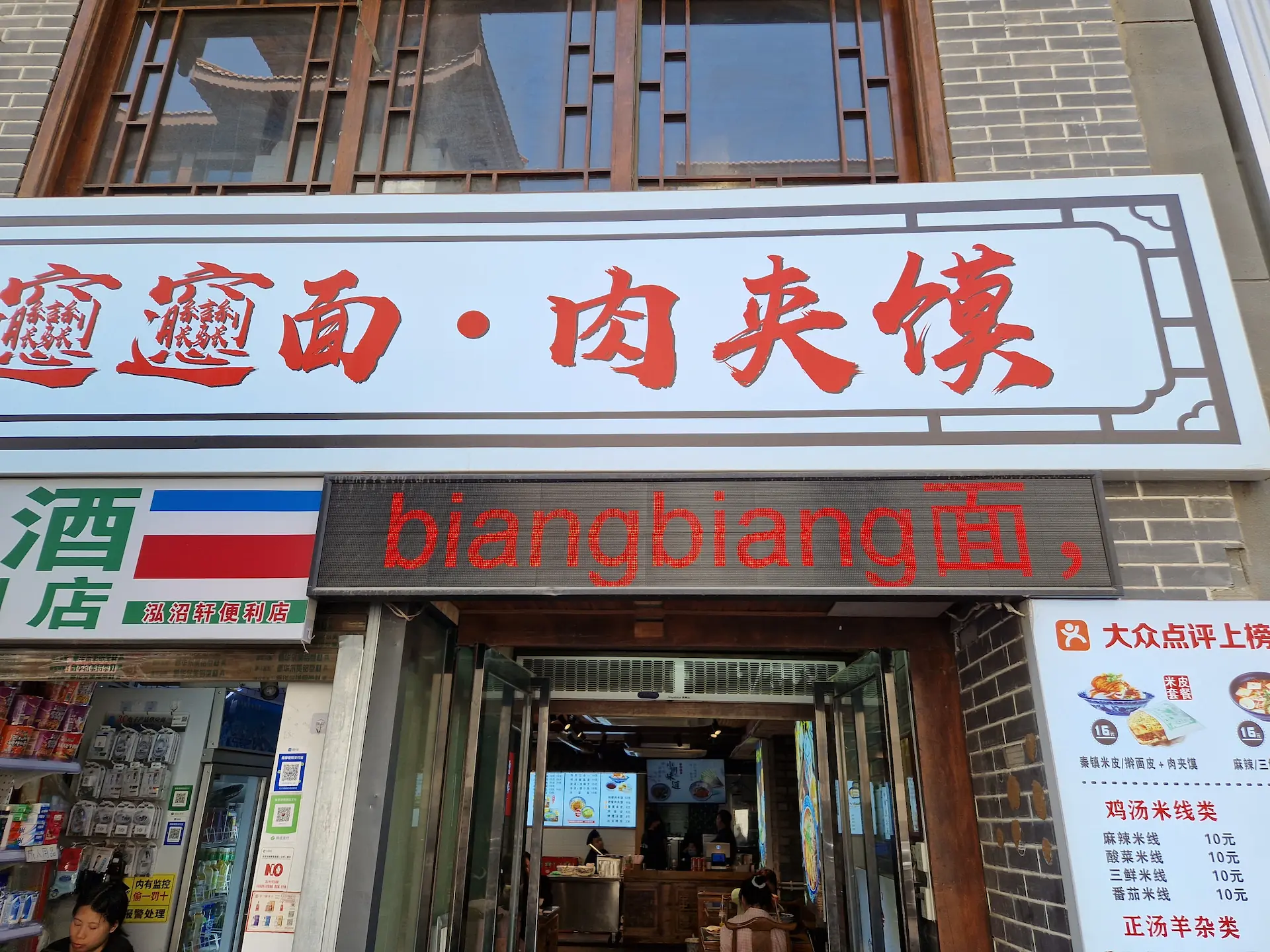 Un signe dans la rue annonce des nouilles biángbiáng, avec les caractères 'biáng' romanisés et le caractère 'miàn' (nouilles) en chinois