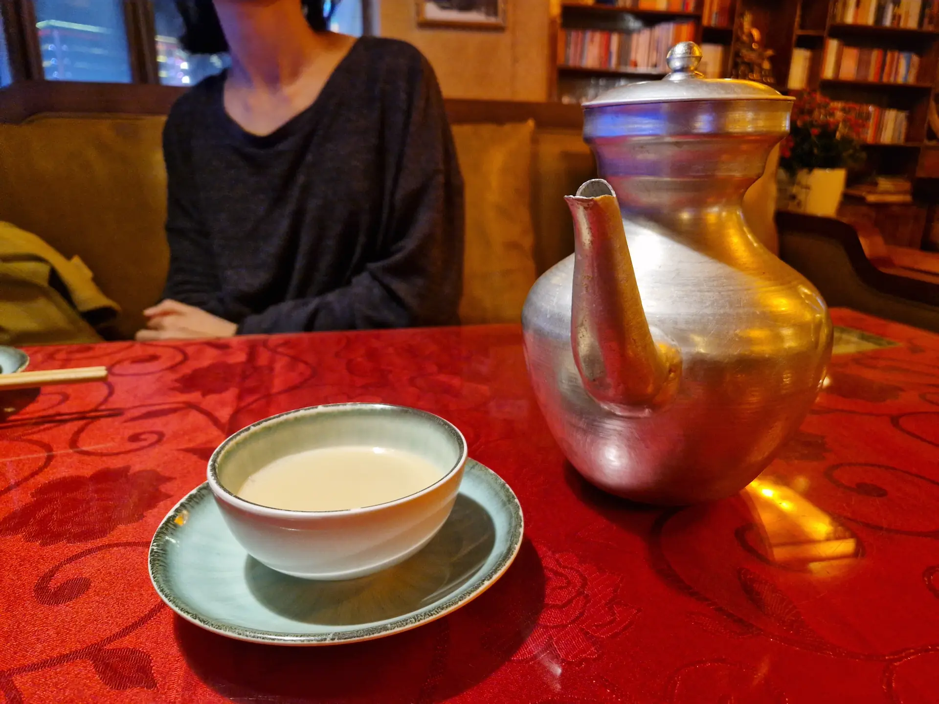 Une grande carafe métallique et une tasse en céramique remplie d'une boisson blanc opaque, le thé au beurre tibétain