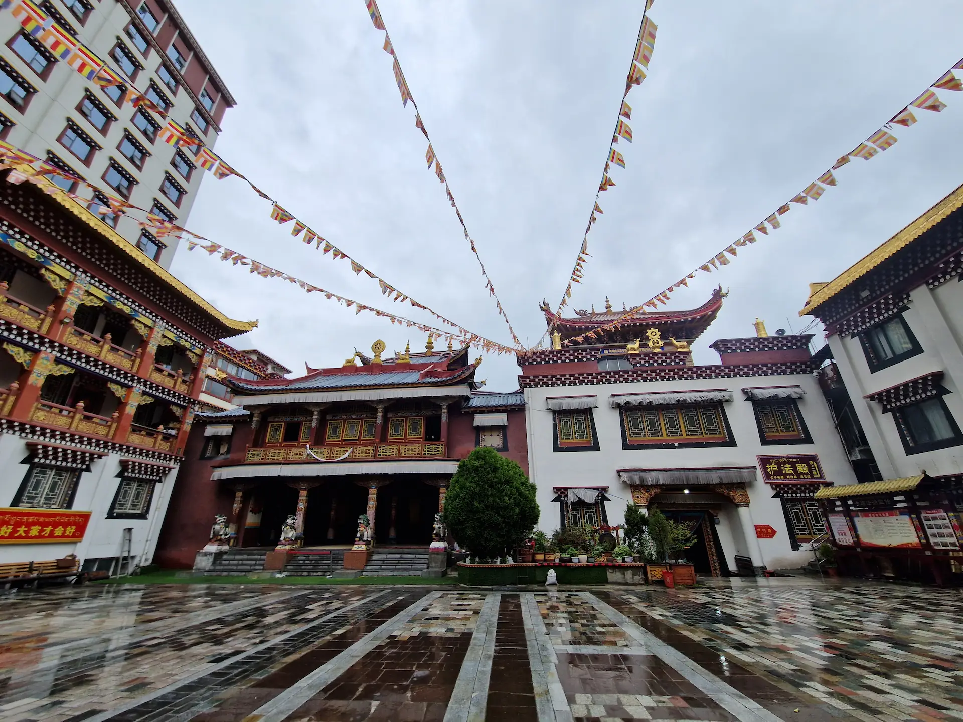 La cour d'un monastère à ciel ouvert, traversée de guirlandes de drapeaux de prières "loungta"
