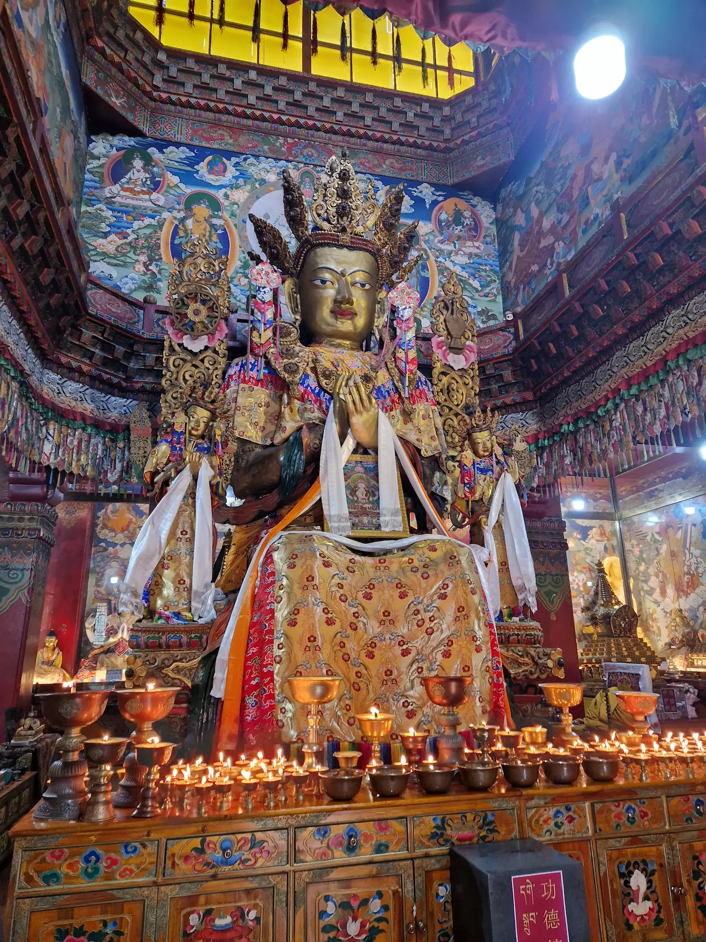 Des dizaines de petites bougies allumées devant une grande statue colorée au milieu du temple