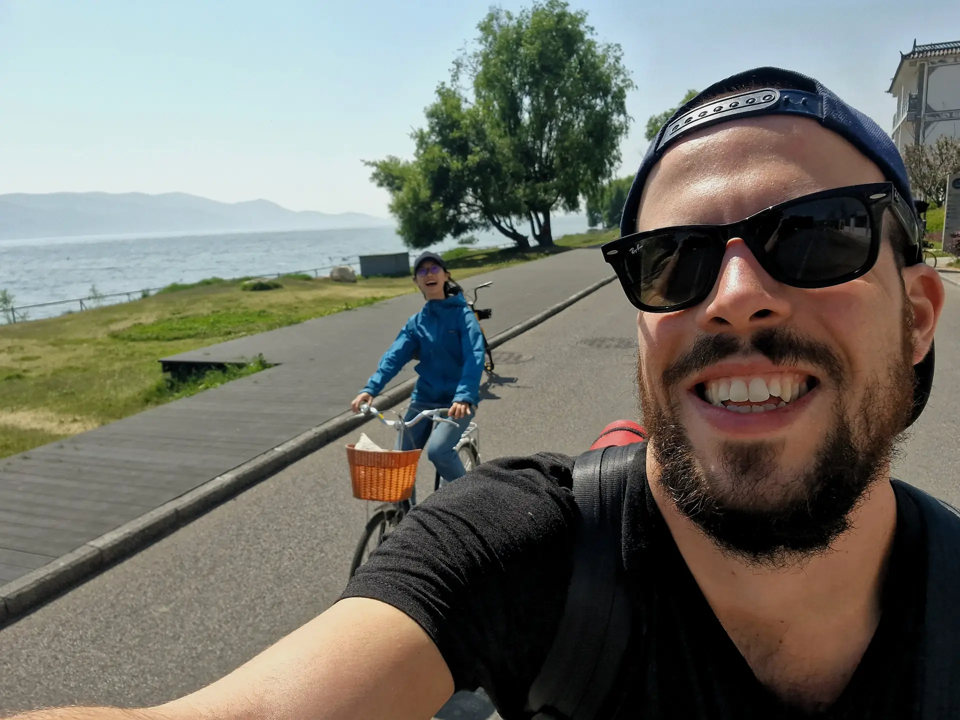 Robin et Clara à vélo se prennent en selfie au bord du lac. Ils ont de grands sourires.