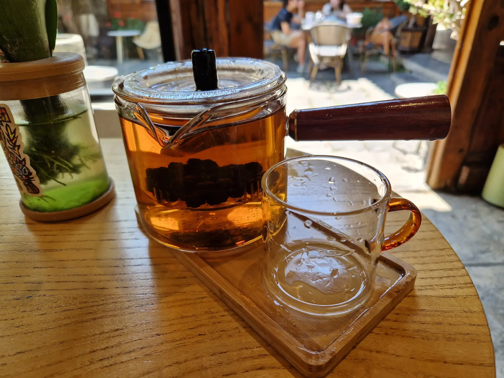 Le thé est servi dans une théière en verre, avec une poignée en bois sur le côté.
