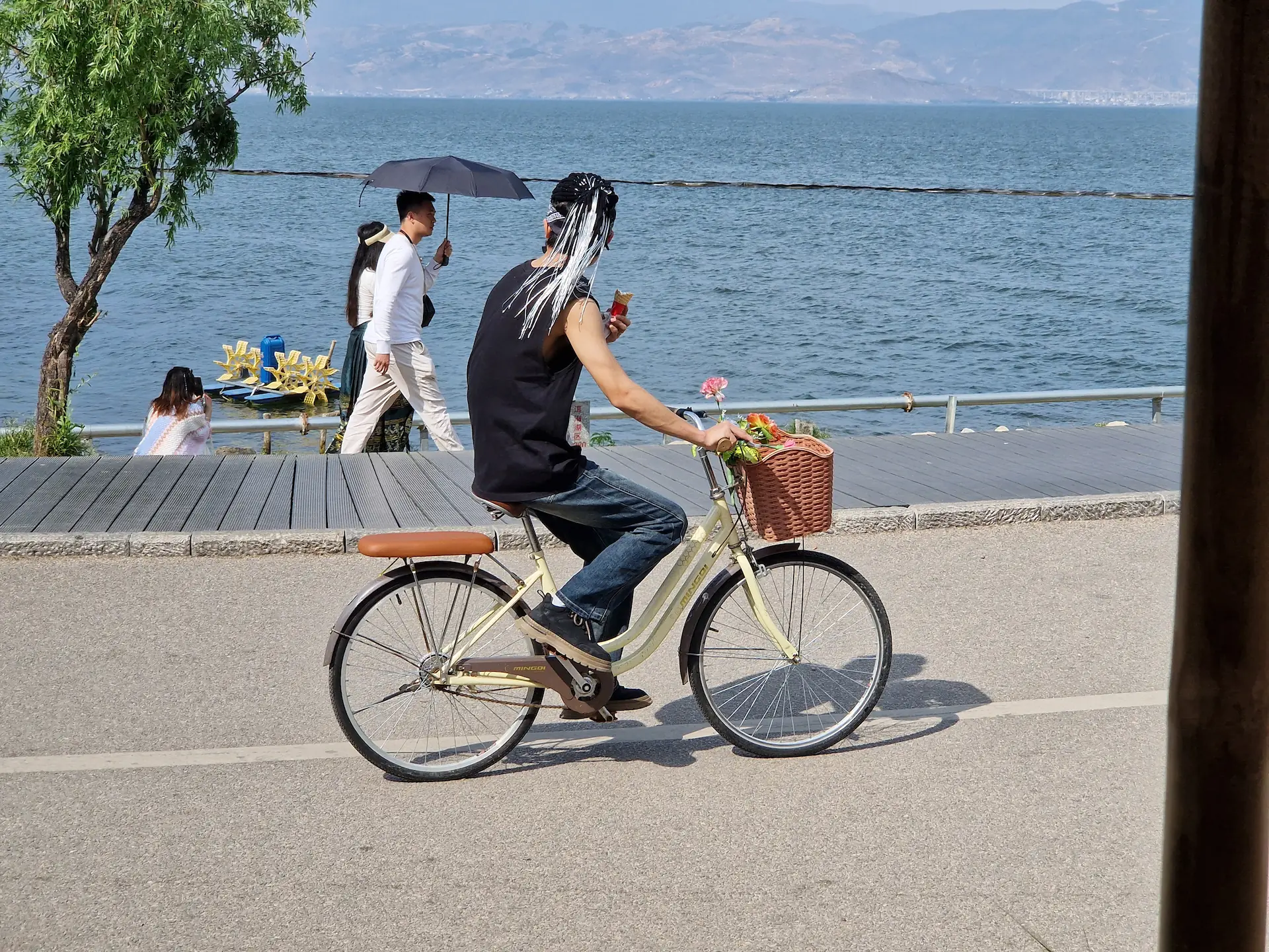 Un 'hippie' à fausses dreads est sur un petit vélo avec une glace à la main.