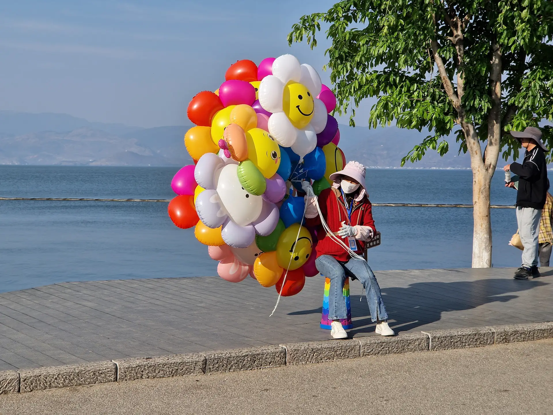 Une dame vend des ballons en forme de fleurs qui font de grands sourires.