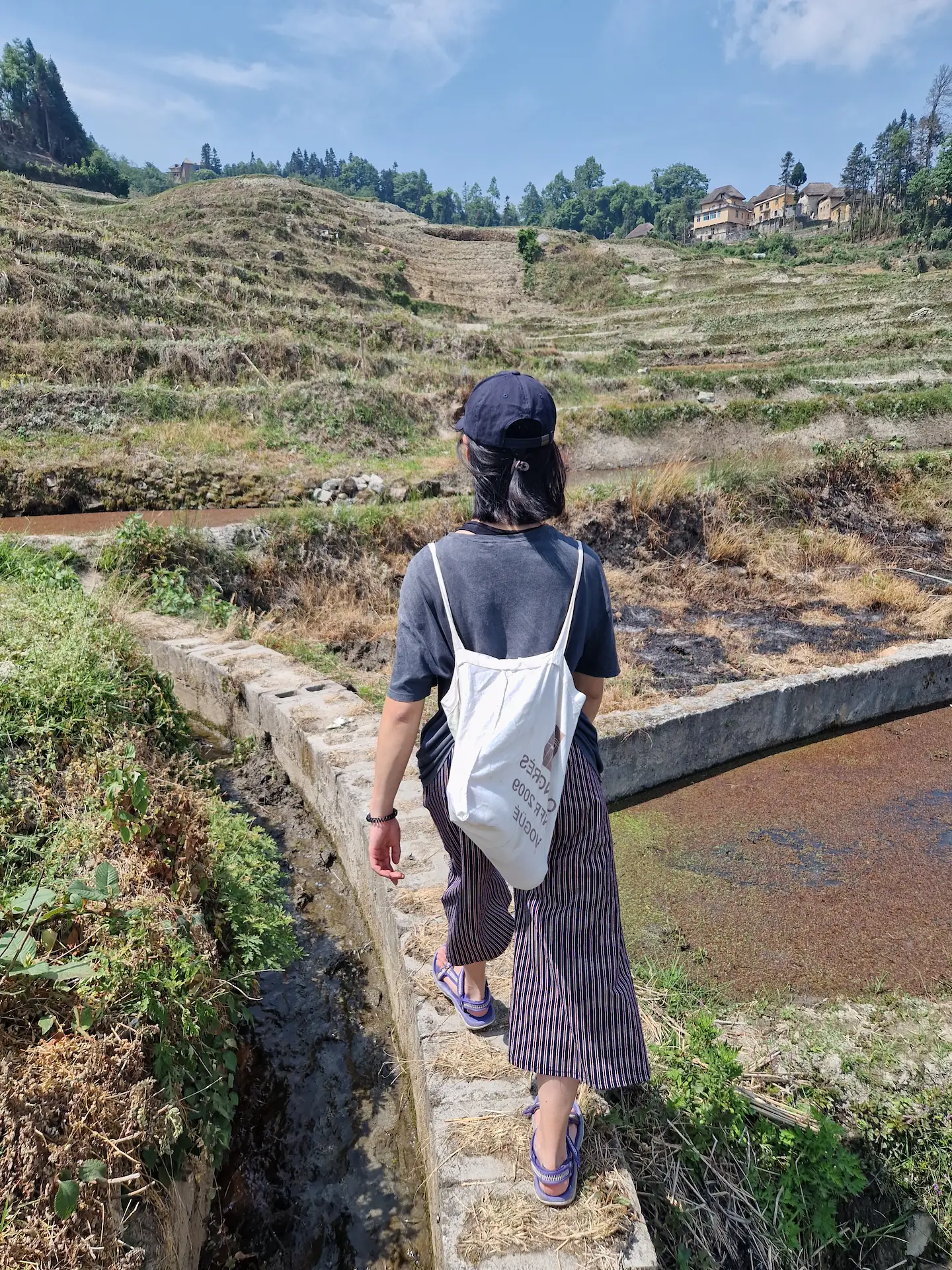 Clara marche sur une section bétonnée entre deux rizières.