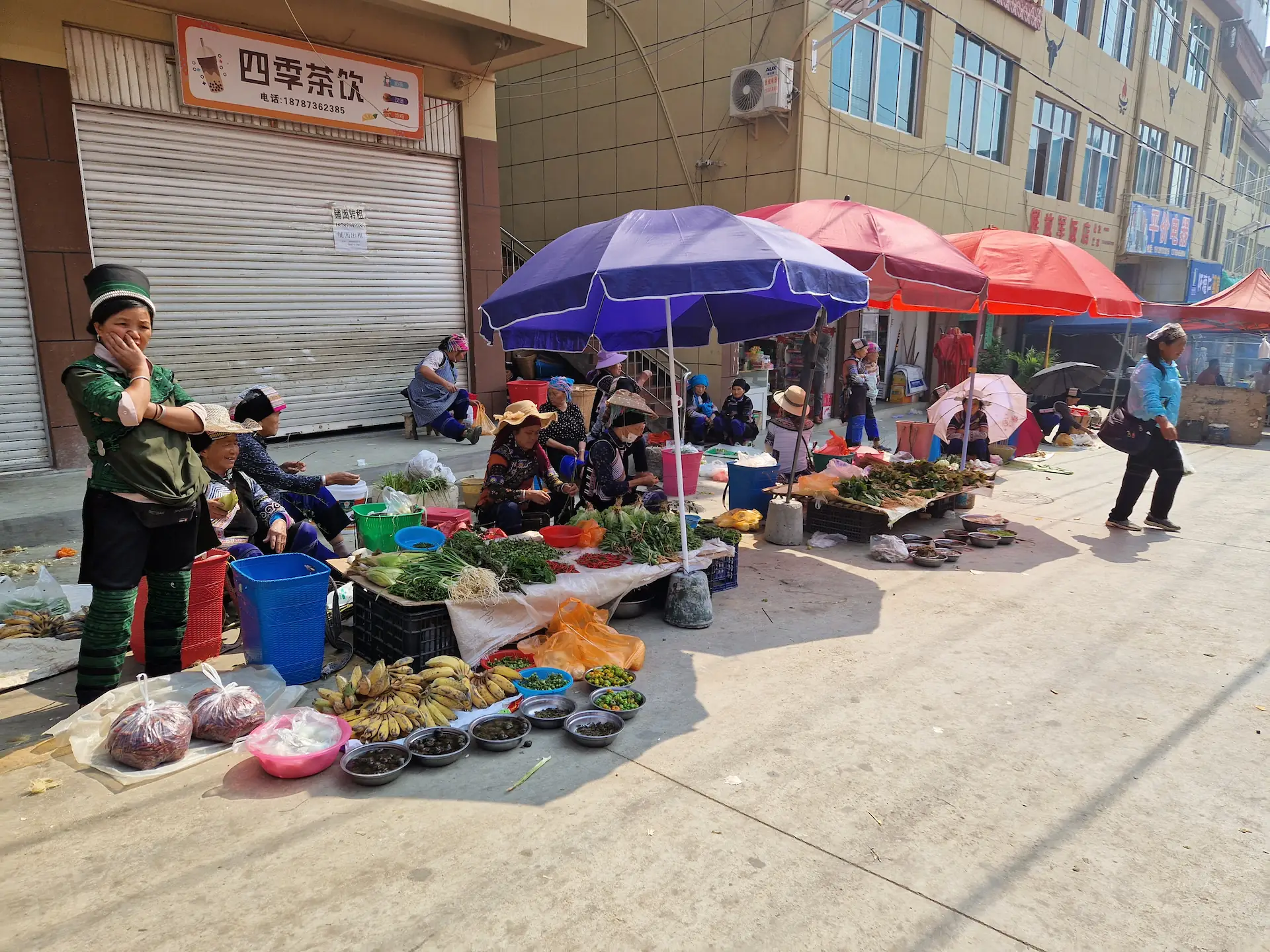 Des vendeuses en habits traditionnels proposent leurs légumes et produits à même le sol. Quelques parasols sont ouverts pour les protéger du soleil.